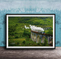 A framed photograph depicting a steam train traveling on a stone bridge over a lush, green valley.