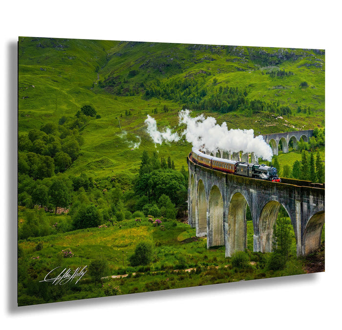 A steam train travels along a stone viaduct, surrounded by lush green hills and trees.