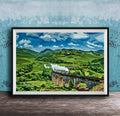 A framed painting depicting a scenic landscape with a curved stone bridge spanning a valley, surrounded by rolling hills and lush greenery.