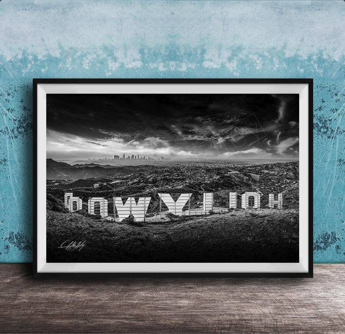 A black and white photograph of the Hollywood Sign, a famous landmark in Los Angeles, California. The sign is prominently displayed in the foreground, with the city skyline visible in the background.