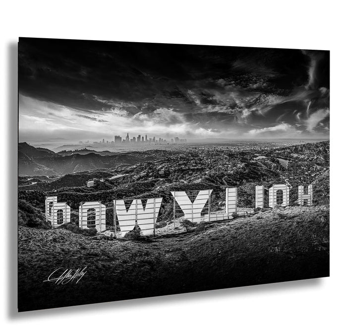 The image is a black and white photograph of the Hollywood Sign, a famous landmark in Los Angeles, California. The sign is prominently displayed in the foreground, with the city skyline visible in the background. The sky above the sign is filled with clouds, creating a dramatic and moody atmosphere. The image is a striking and visually appealing composition, capturing the iconic Hollywood Sign and the surrounding landscape.