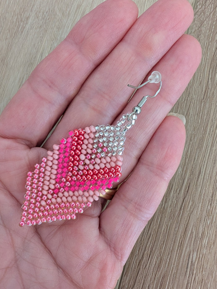 Pink beaded earrings held in a hand on a wooden surface