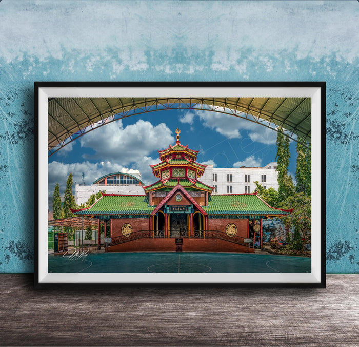 A framed photograph of a traditional Chinese temple with a red roof and green walls, set against a blue sky with clouds.