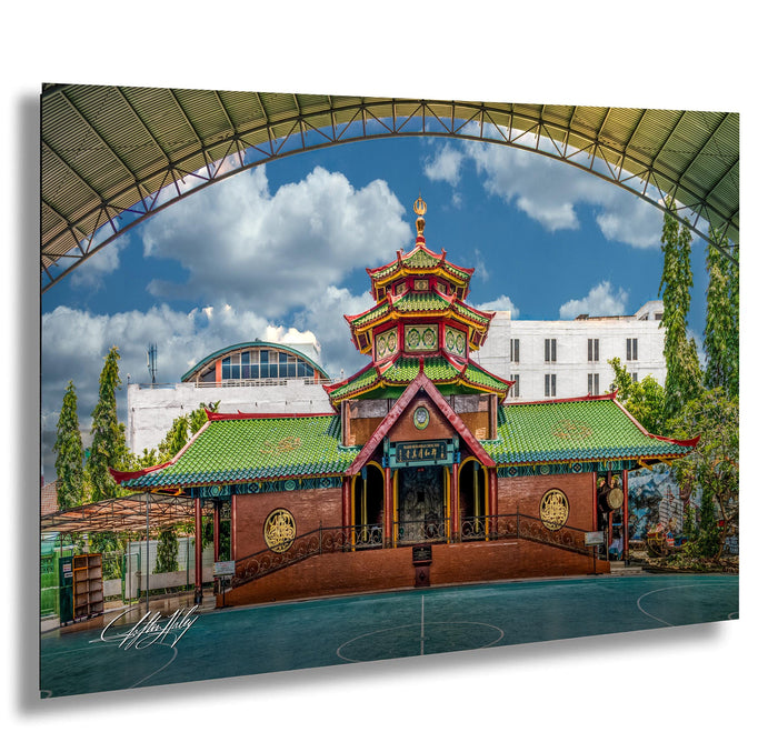 A colorful and ornate Chinese temple with a green roof and red walls, surrounded by trees and a large arched structure in the background.
