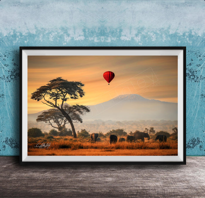 A framed photograph depicting a serene landscape with a lone tree, a herd of elephants, and a red hot air balloon floating in the sky, all set against a backdrop of a majestic mountain range.