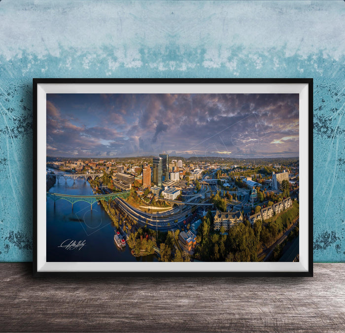 The image is a framed aerial view of a cityscape, showcasing a mix of buildings, roads, and a river.