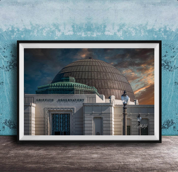 the Griffith Observatory, a large domed building with a distinctive architectural style, set against a dramatic sky with clouds and a sunset.