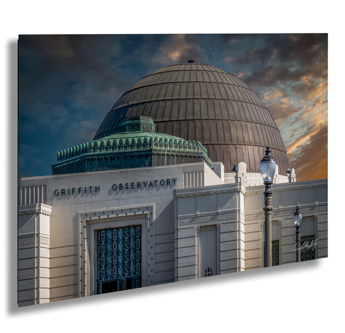 the Griffith Observatory, a large domed building with a distinctive architectural style, set against a dramatic sky with clouds and a sunset.