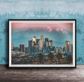 A framed photograph of the Los Angeles skyline at sunset, with the city's skyscrapers and mountains in the background.