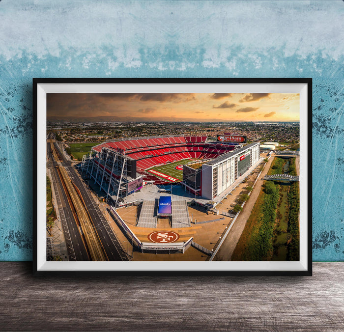 The image is an aerial view of a large sports stadium, likely the 49ers stadium, with its distinctive red roof and surrounding landscape.