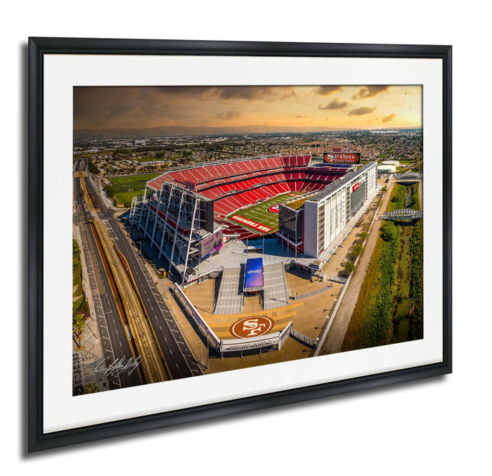 An aerial view of a large sports stadium with a red roof and white walls, surrounded by a cityscape.
