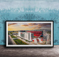 The image is a framed photograph of a large stadium with a red roof, set against a backdrop of a blue sky with clouds.