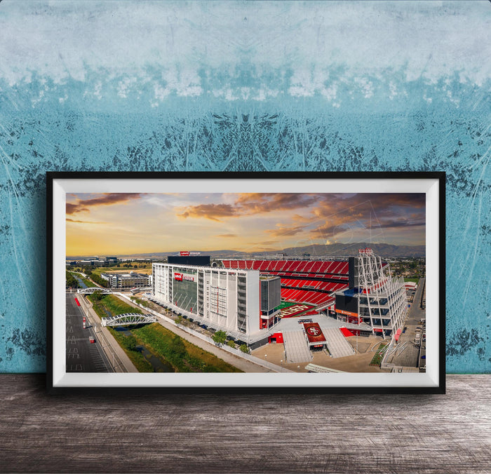 The image is a framed photograph of a large stadium with a red roof, set against a backdrop of a blue sky with clouds.