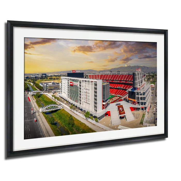 The image is a framed picture of a large stadium with a red roof, surrounded by a cityscape with buildings and a bridge.