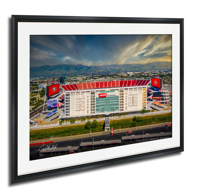 a large stadium with a red roof and various advertisements, surrounded by a cityscape and mountains in the background.