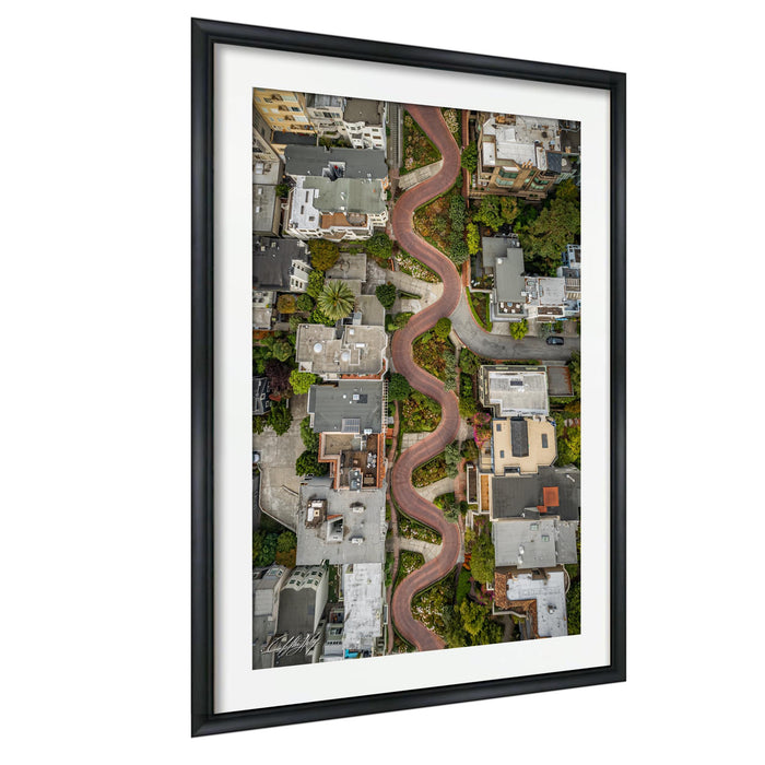 The image is an aerial view of a winding road that curves through a densely populated urban area, with buildings and greenery lining the sides of the road.