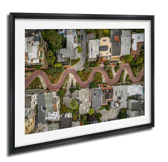 The image is an aerial view of a winding road that curves through a densely populated urban area, with buildings and greenery lining the sides of the road.