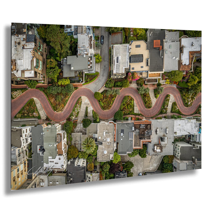 The image is an aerial view of a winding red road that curves through a residential neighborhood, with houses and trees lining the sides of the road.