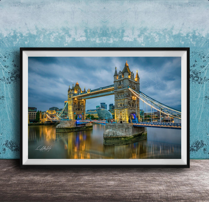 A framed photograph of the iconic Tower Bridge in London, England, illuminated at night against a cloudy sky.
