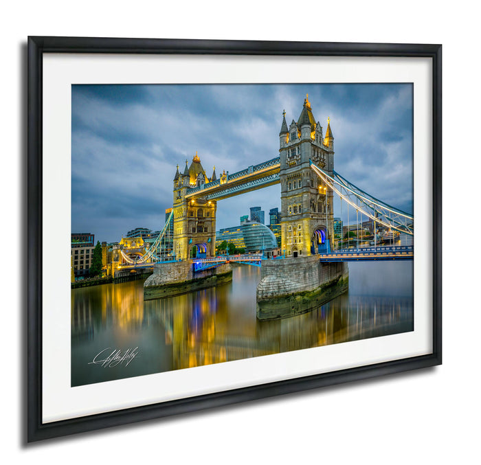 A framed photograph of the iconic Tower Bridge in London, England, illuminated at night against a cloudy sky.