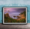 A framed photograph depicting a serene coastal landscape with a lone tree on a rocky cliff overlooking the ocean at sunset.