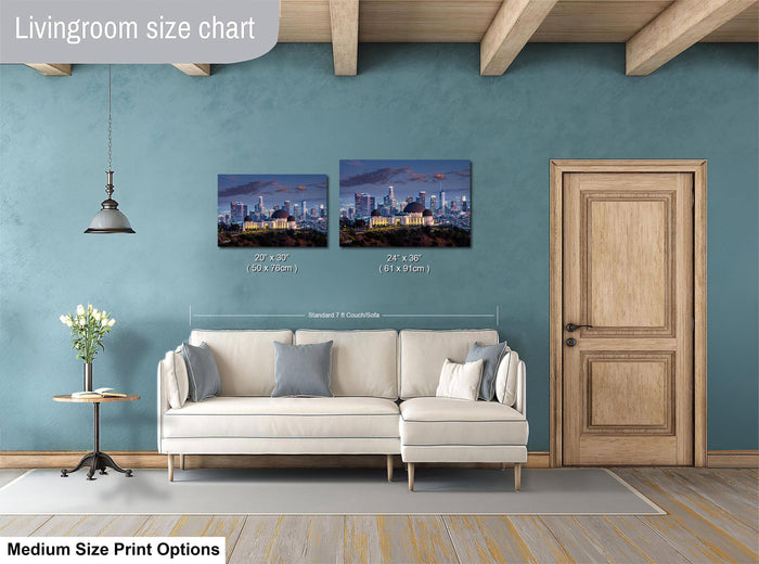 a living room with a white sofa and a wooden door. Above the sofa, there are two framed pictures of a city skyline, likely representing Los Angeles. The living room has a blue wall and a wooden ceiling.