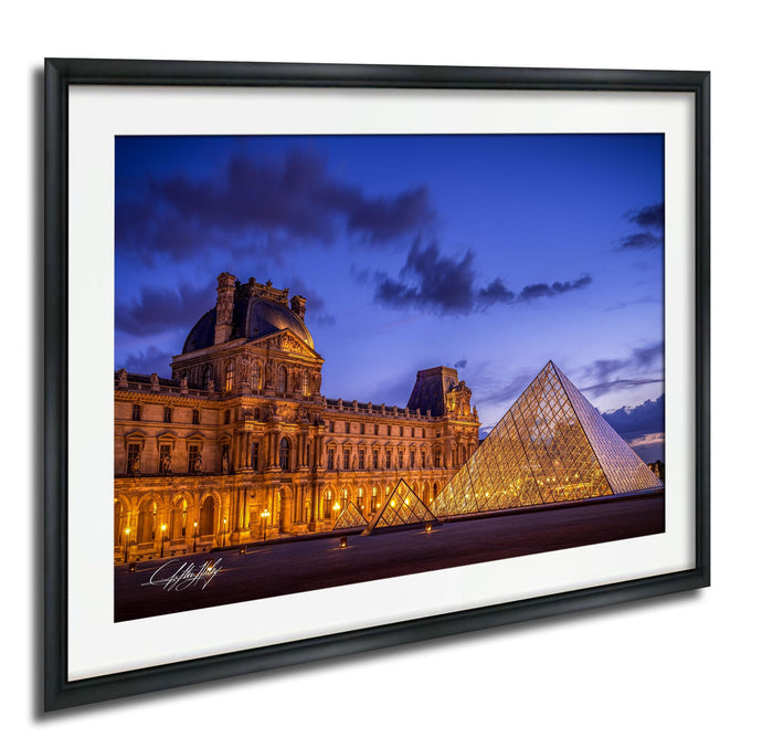 the Louvre Museum in Paris, France, with its iconic glass pyramid structure illuminated against a dark blue sky.