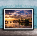 a picturesque scene of a river with a bridge, set against a stunning sunset sky with clouds.