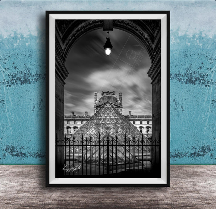 A framed black and white photograph of the Louvre Museum in Paris, France, with the iconic glass pyramid structure of the museum prominently featured.