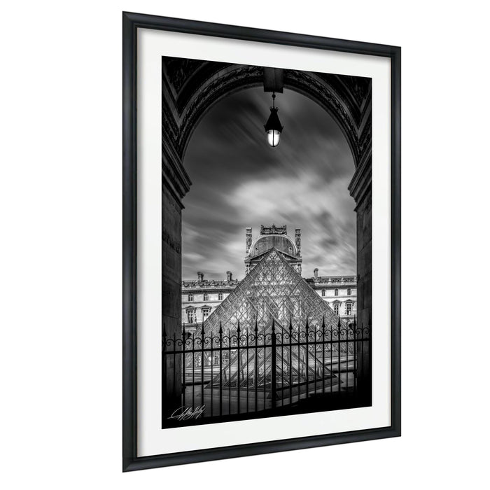 A black and white photograph of the Louvre Museum in Paris, France, with the iconic glass pyramid structure of the museum prominently featured.