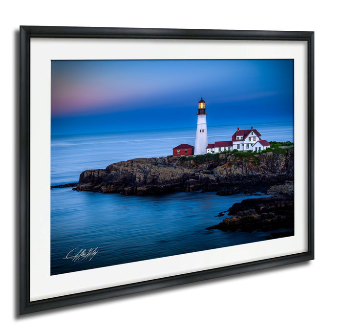 A framed photograph depicting a lighthouse on a rocky coastline, with the ocean in the background.