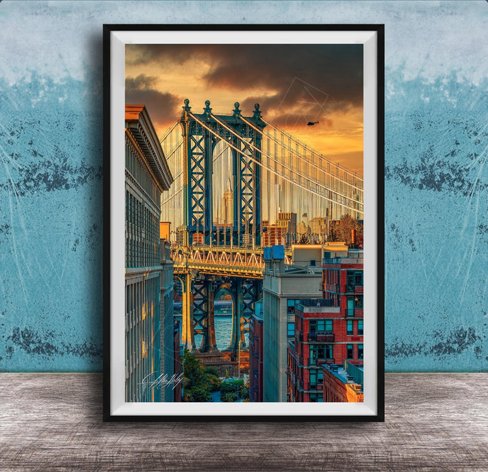 The image is a framed photograph of the Manhattan Bridge in New York City, with the bridge and surrounding buildings illuminated by a colorful sunset sky.