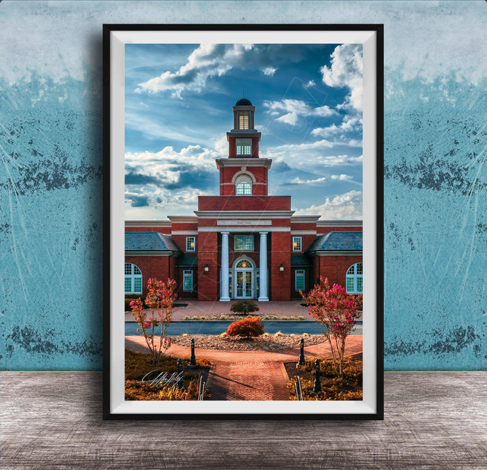 A framed photograph of a red brick building with a prominent clock tower, set against a blue sky with clouds.