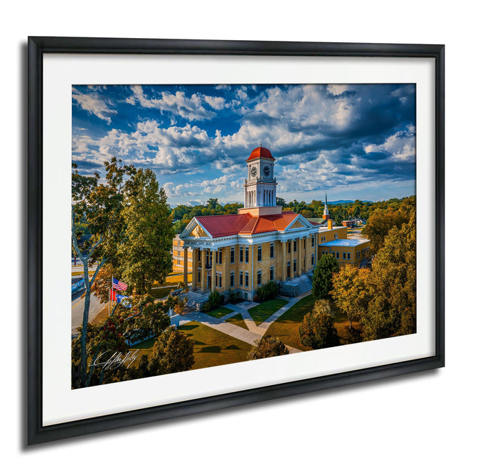 A framed aerial view of a historic building with a clock tower, surrounded by trees and a grassy area.