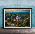 A framed aerial view of a historic building with a red roof, surrounded by lush greenery and mountains in the distance.