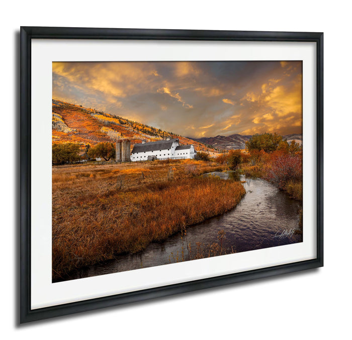 a picturesque rural landscape with a farmhouse nestled among rolling hills and a winding stream. The sky is filled with vibrant orange and yellow clouds, creating a warm and inviting atmosphere. The overall scene is serene and peaceful, showcasing the beauty of nature and the tranquility of the countryside.