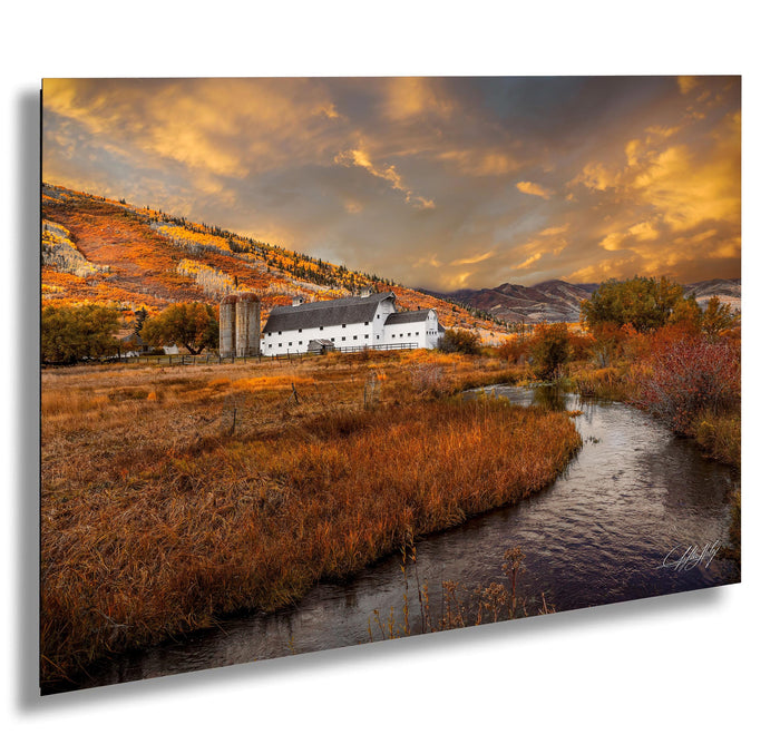 A picturesque rural landscape with a white farmhouse nestled among the rolling hills, a winding stream, and a vibrant autumnal sky.