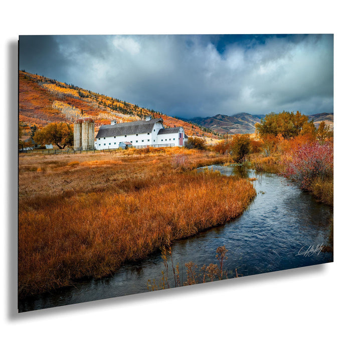 A picturesque rural landscape with a white barn nestled among the rolling hills, a stream meandering through the foreground, and a dramatic sky filled with clouds.
