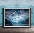 A framed photograph of a large, majestic glacier with a blue-green hue, set against a backdrop of rugged mountains and a serene body of water.