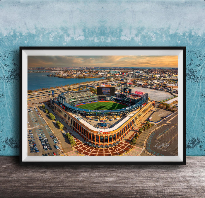 An aerial view of a baseball stadium with a large field, surrounding parking lots, and a body of water in the background.