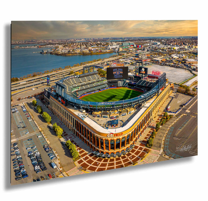 An aerial view of a large baseball stadium with a large field, surrounded by a cityscape and a body of water.