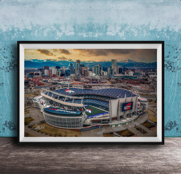 The image is an aerial view of a large sports stadium, likely a football stadium, with the city skyline in the background.