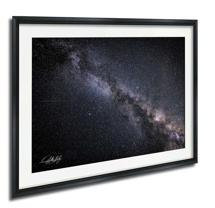 The image is a framed photograph of the night sky, depicting a vast expanse of stars and the Milky Way galaxy.
