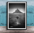 A black and white photograph of a castle or palace situated on a beach, with a body of water in the foreground and a sky above.