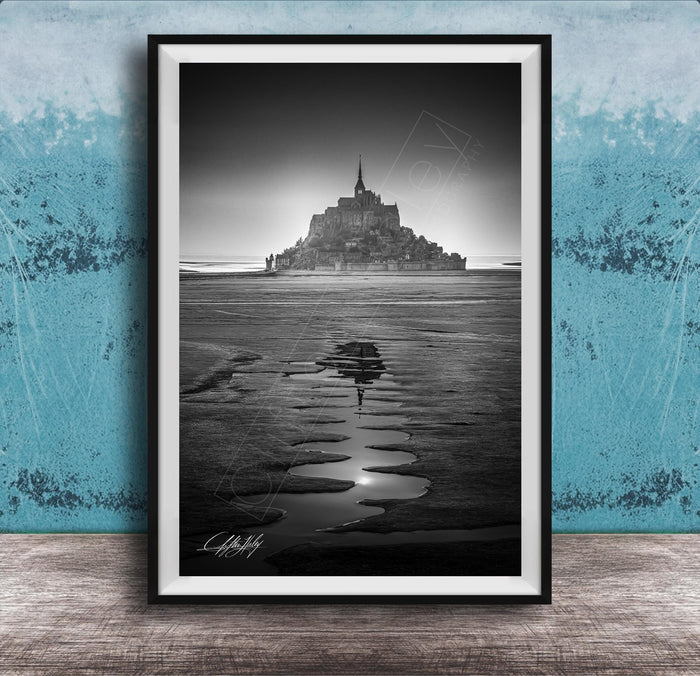 A black and white photograph of a castle or palace situated on a beach, with a body of water in the foreground and a sky above.