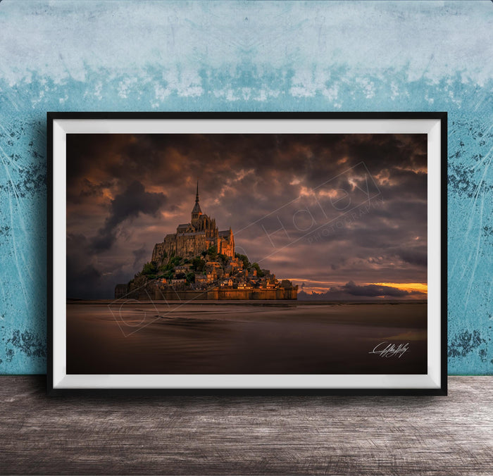 A framed photograph of the iconic Mont Saint-Michel in Normandy, France, with a dramatic sky in the background.