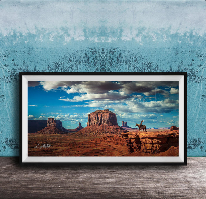 A framed photograph of a desert landscape with a cowboy on a horse, set against a blue and white patterned background.