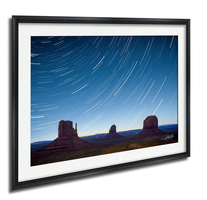 A framed photograph depicting the iconic rock formations of Monument Valley at night, with star trails visible in the sky.