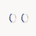 Side view of a pair of silver hoop earrings featuring a vertical channel setting of seven rose-cut deep london blue topaz gemstones, set against a plain off-white background.