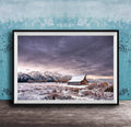 A framed photograph depicting a snowy mountain landscape with a wooden barn in the foreground, set against a cloudy sky.